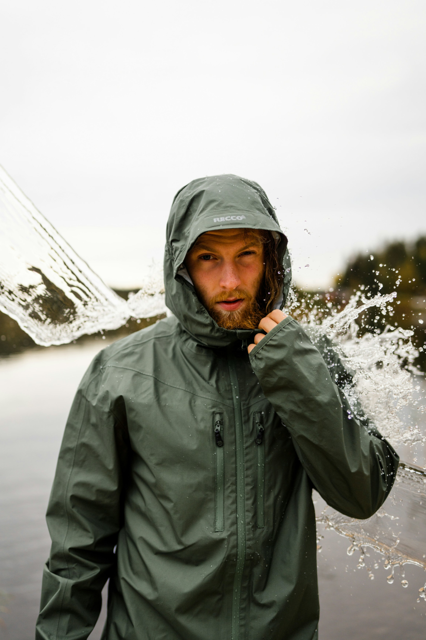 Male model wearing a green rain jacket with the hood up, standing in the rain